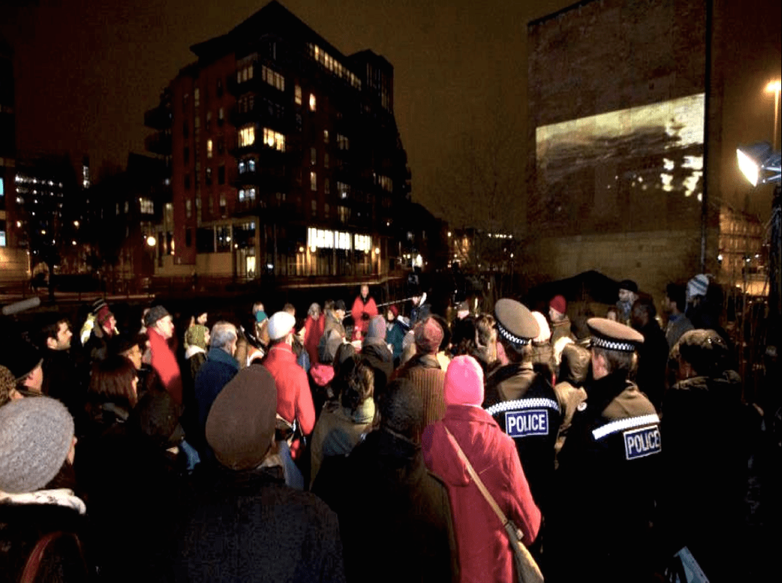 Gathering by the river, Corinne Silva’s film Wandering Abroad projected onto an exterior wall.